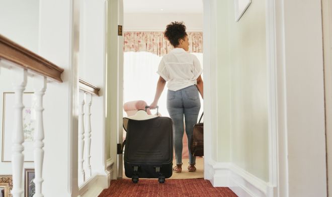 Rearview shot of an attractive young woman walking into a hotel room with her luggage in tow