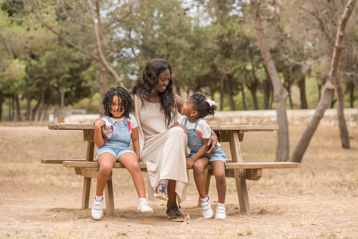 Mother and kids enjoying time together while relaxing sitting on a bench outdoors in a park.
