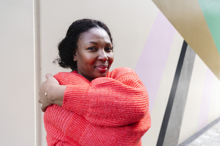 Smiling woman wearing orange sweater hugging self