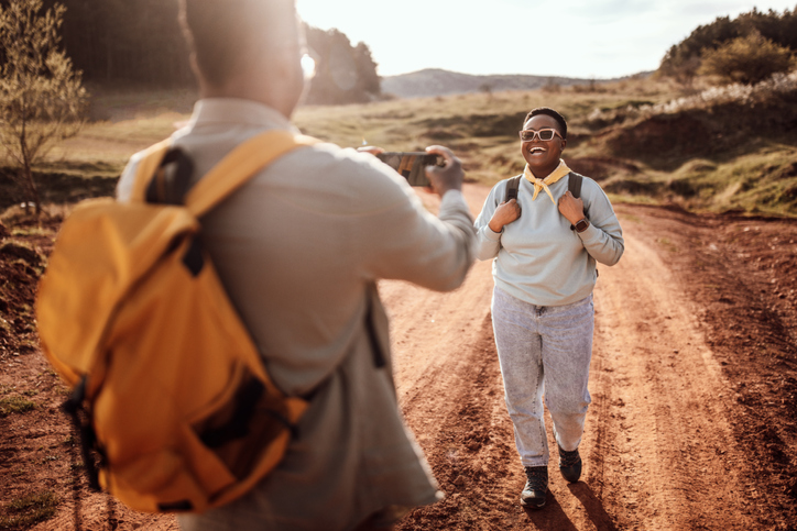 Rear view of male backpacker photographing girlfriend