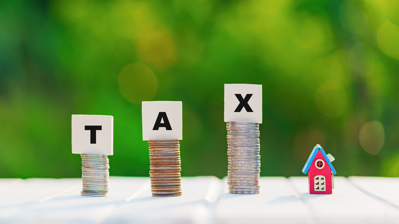 Estate tax. Property tax concept with wooden block on stacked coins. Model house with stack of coins money and tax on green background. Business investment