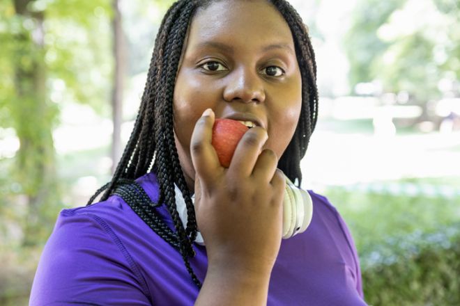 A young girl resting after exercising eats an apple and looks at the camera in the park