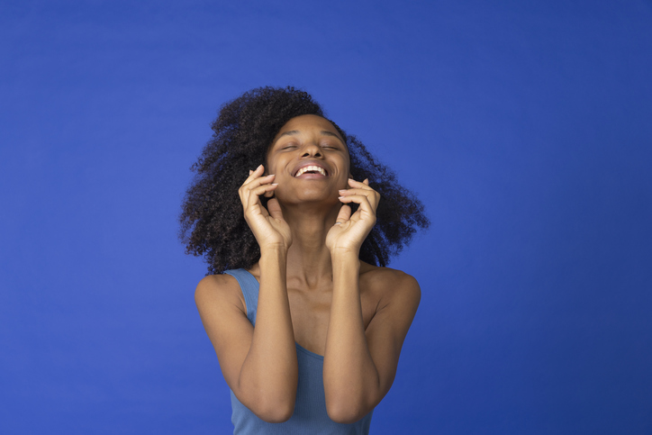 Young woman with eyes closed laughing against blue background