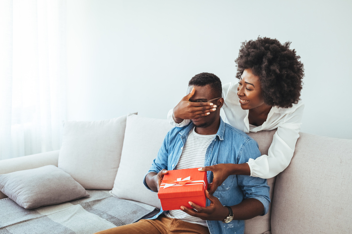Wife making a surprise giving a present to her husband at home