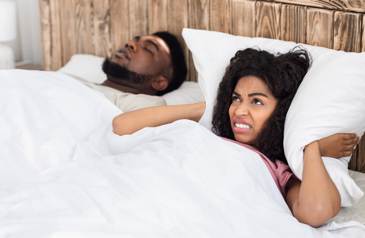 Angry black woman covering her ears with pillow considering a sleep divorce
