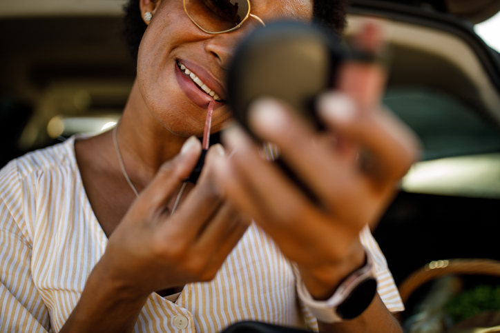 Woman looking in the little hand mirror, applying lipstick and talking on the phone