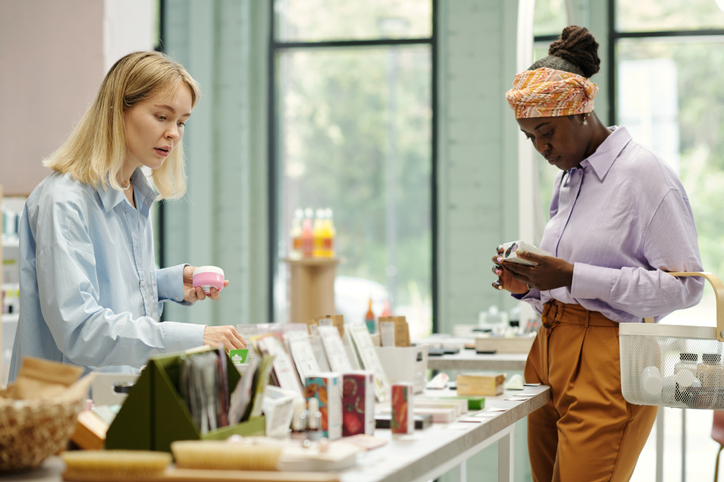 Two young female customers choosing makeup products on discount display