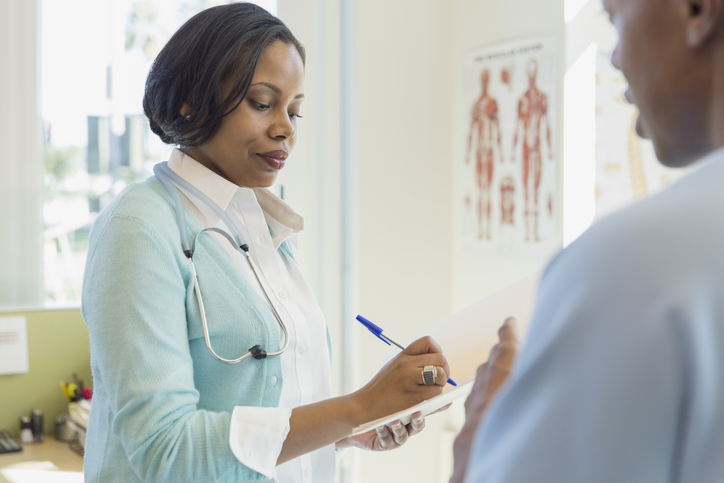 Female doctor writing in file while talking with patient in clinic