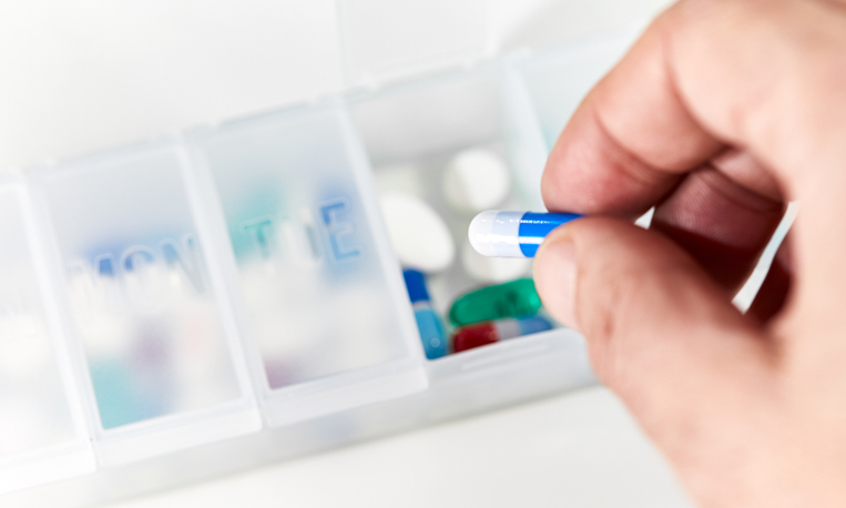 Close-up of a man's hand taking a capsule medicine out of a pill box, managing medication