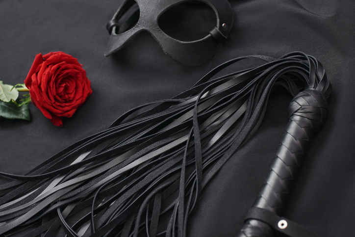 Role playing. Top view of bdsm leather kit ( black whip and mask) with red rose on black silk hanky panky gifts