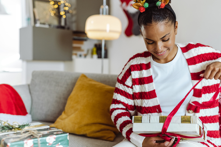 Young beautiful smiling woman unwrapping Christmas gift at home