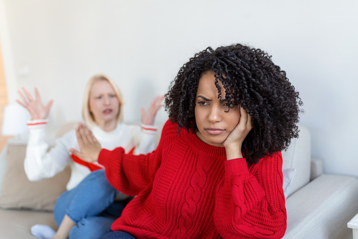Dont want to hear. Unhappy disturbed tired woman communicating with her friend sitting near her on the sofa shaking her hands. Friends arguing on sofa at home. Two female friends arguing not showing emotional maturity