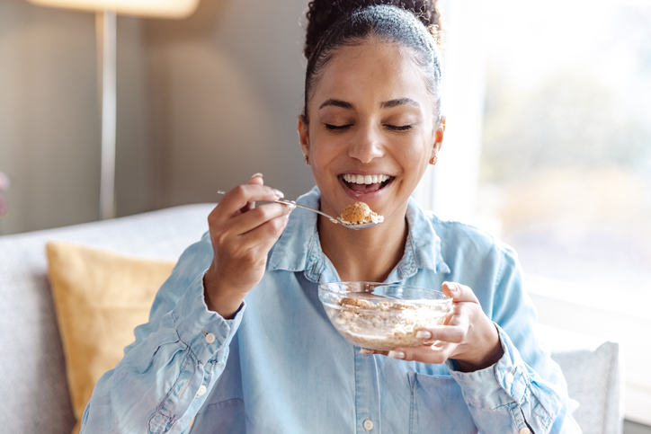 Happy young woman eating cereals for breakfast at home trying the blood type diet