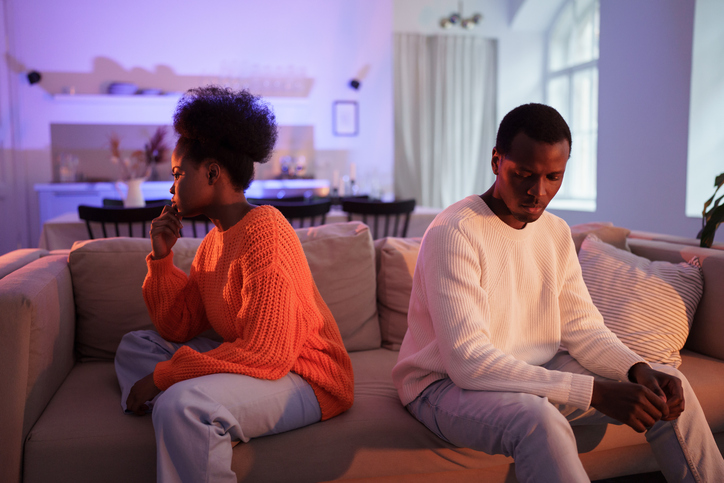 Upset african couple have problems in marriage, sitting back to back on sofa at home and not talk