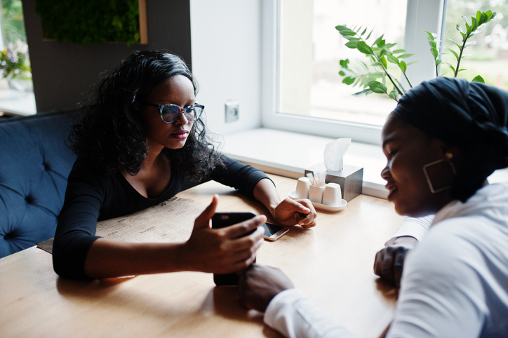 Two young women talking while sitting at table in loft office who have different communication styles