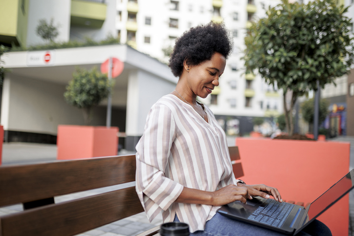 Businesswoman working on laptop and drinking coffee at the public park