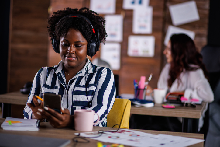 Young woman taking a break from work at her desk and scrolling through social media via smart phone