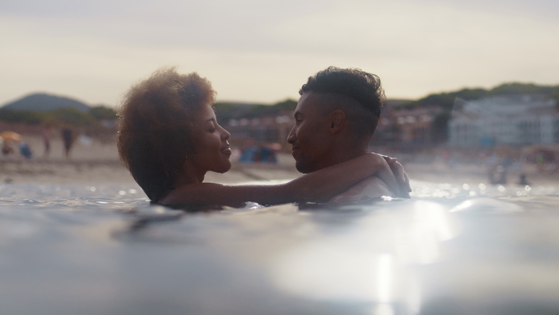 Romantic heterosexual african ethnicity couple swimming in the sea together. Embracing each other