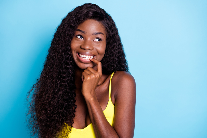 Portrait of attractive cheerful wavy-haired girl biting nail thinking copy space isolated over vibrant blue color background