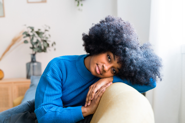 Cheerful black woman sitting on couch enjoying being selfish