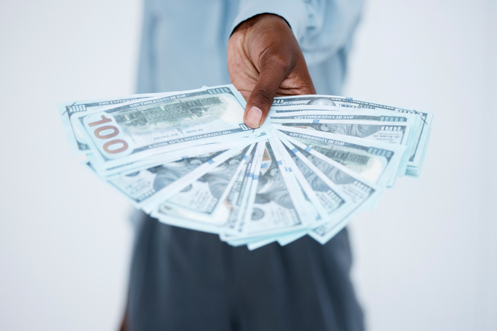 Close up of business woman's hands holding banknotes fanned out. Woman offering to give a stack of money for business opportunity or to invest against studio background. Successful and profitable business