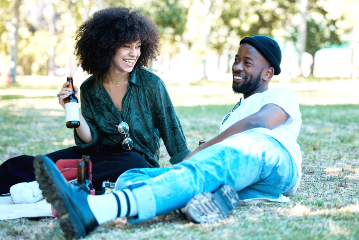 Interracial couple in nature park together, man and woman relax with drink on grass and happiness for people on picnic date outside. Happy black friends dating, laughing and having fun on weekend on valentine's day