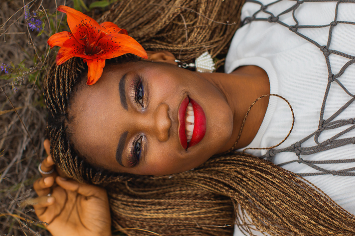 Beautiful african woman in white shirt and cape on nature background. Authentic style. Stylish accessories. Beauty portrait. Earrings. Fashion style. Model lie on grass. Red lips