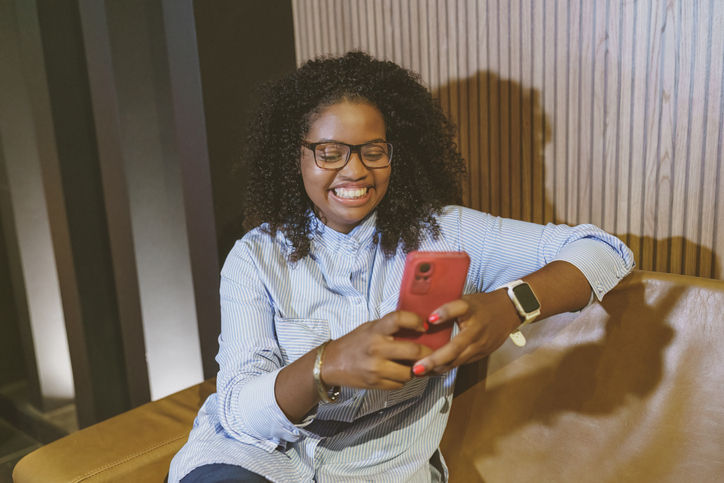 Portrait young black woman sitting on sofa and texting on cell phone