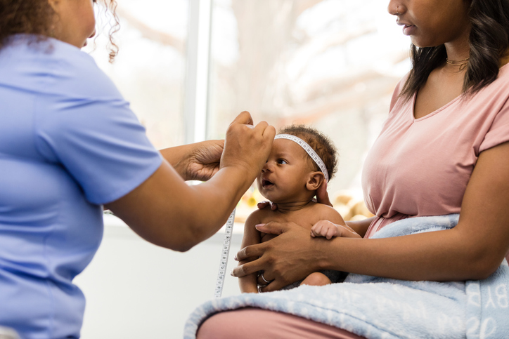 Female doctor measures circumference of tiny baby's head in maternity ward with Black mother