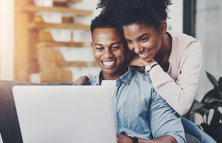 Black couple, hug and happy with laptop in home for remote work, reading email or scrolling social media on sofa. People, embrace and technology in living room for online browsing and watching movie