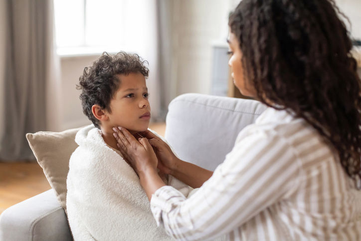 Concerned black mother gently touching her son's throat, checking signs of illness