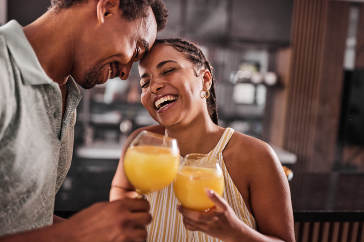 Cheerful black couple toasting with juices at home.