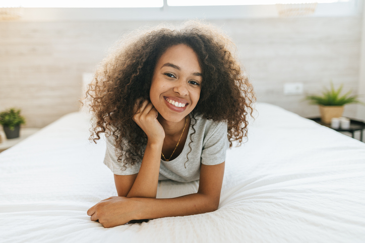 Portrait of woman with curly hair lying on bed