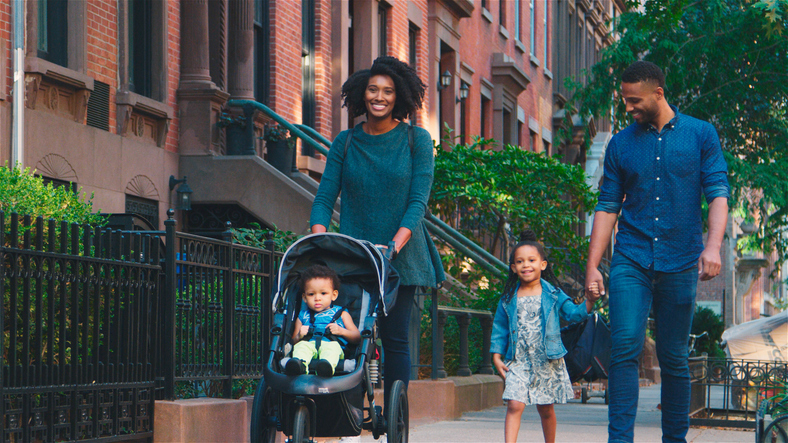 Family Day Out With Mum Pushing Baby In Buggy As They Walk Along Urban Street In New York City USA