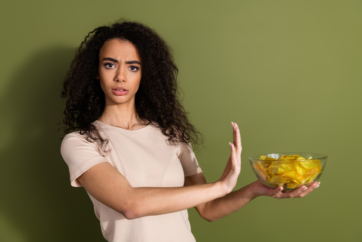Photo of serious dissatisfied girl with wavy hairdo dressed beige t-shirt give up chips say stop isolated on khaki color background