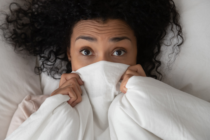 Young black woman peer out of white fluffy duvet
