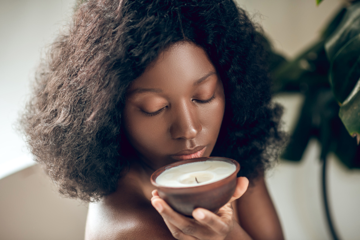 Naked dark-skinned woman smelling an organic candle