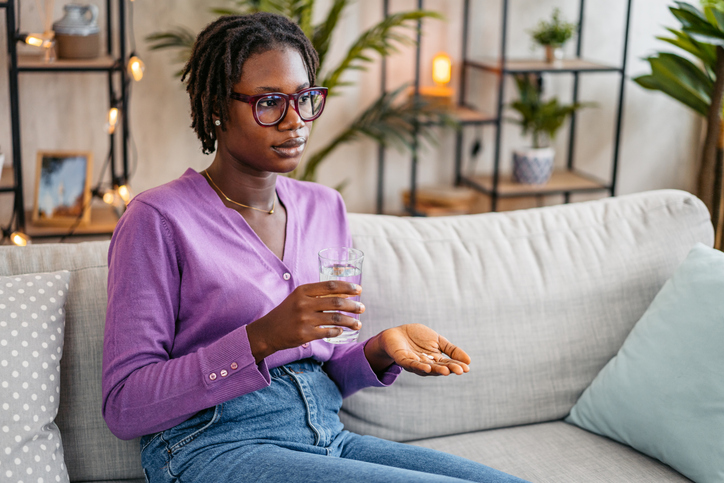 Young Woman Taking Medicine Pills With A Glass Of Water