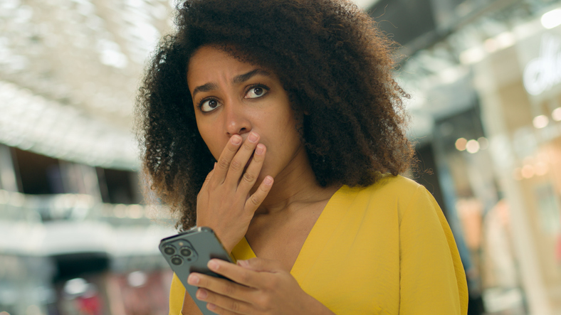 African American woman looking smartphone mobile phone screen holding head bad news problem notification upset girl sad female worried anxiety frustrated online anxious broken deception shopping mall
