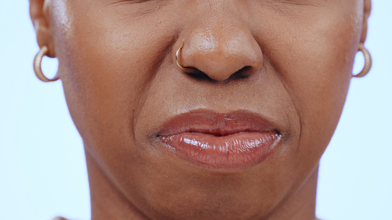Woman, face and closeup of nose and mouth in studio with disgust for bad smell, dislike scent or air. Person, negative facial expression or reaction to sweat, nausea or aroma on blue background