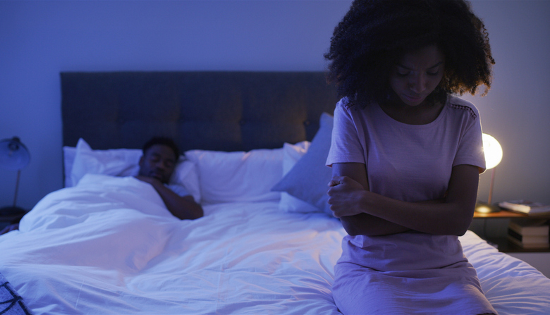 Sad, woman and bed with African couple, night and marriage problem from infertility with stress from fight. Bedroom, sitting and thinking of divorce and relationship conflict at home with insomnia