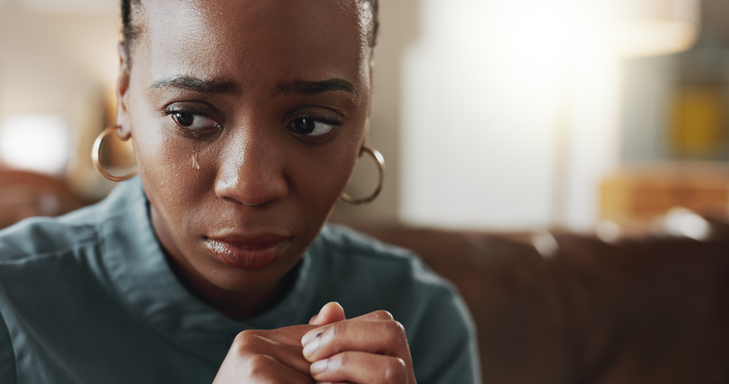 Crying, sad and black woman with depression, thinking or psychological trauma in home living room. Tears, unhappy or African person with anxiety for crisis, mental health challenge or stress for ptsd