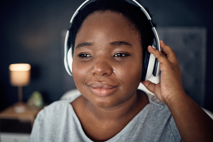 Crying, sad and black woman with headphones for music, sound or audio. Tears, radio and plus size African person listening, hearing and streaming podcast with depression, crisis and problem in home