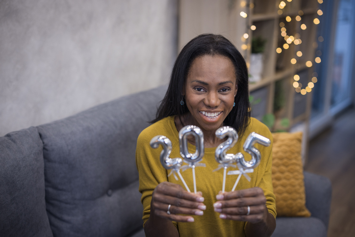 Woman holding balloons shaped as numbers 2025 and smiling