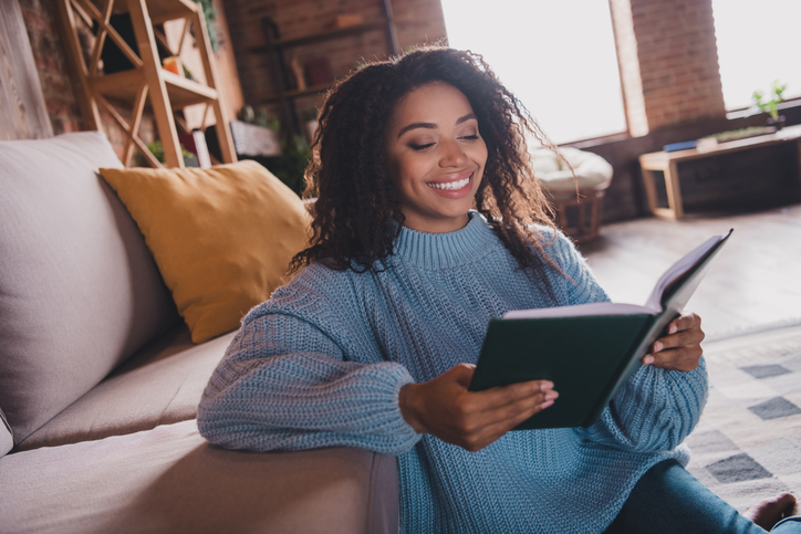 Young woman enjoying leisure time reading a book at home interior during daylight
