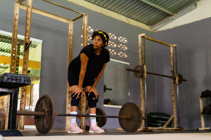 Determined young adult woman resting after weightlifting in old gym