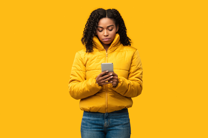 Serious African Girl Using Smartphone Wearing Winter Clothes, Studio Shot