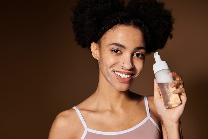 Young woman showcasing skincare routine while smiling confidently indoors in soft lighting