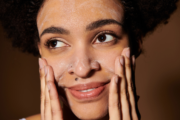 Young beautiful woman applying facial cleanser while smiling in a serene setting