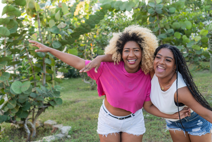 Two happy friends embracing and pointing in a park, showing their happiness and excitement